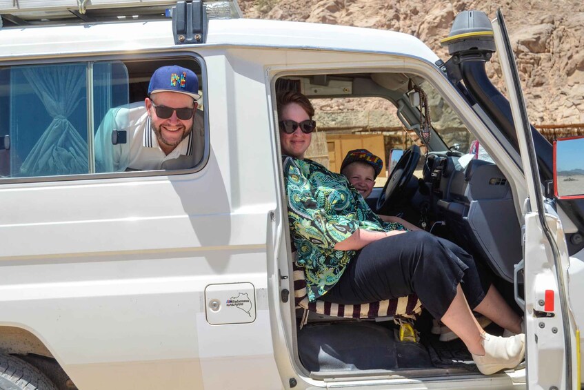 A white vehicle with its door open, revealing two people inside and a child in the back. 3