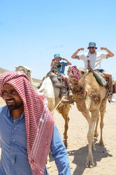A man in traditional attire leading two camels, each carrying a passenger. 2