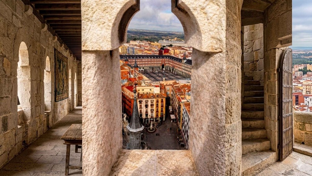 A stone corridor with an arched window overlooking a historic cityscape. 4