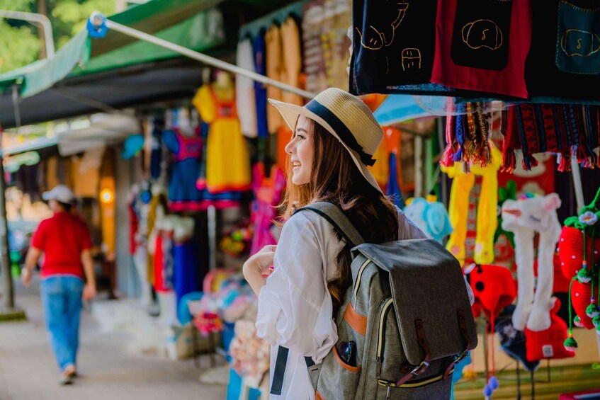 A person wearing a straw hat and carrying a backpack, walking past a market stall with colorful items. 2