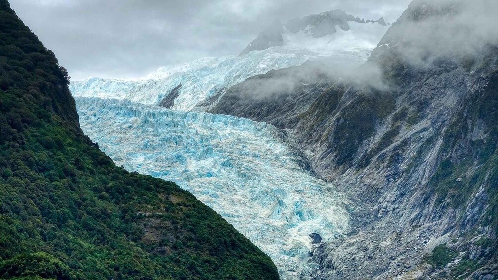 A glacier in a mountainous area with steep cliffs and dense vegetation. 1