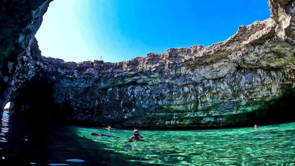 A clear blue cave entrance with water and people swimming inside. 3