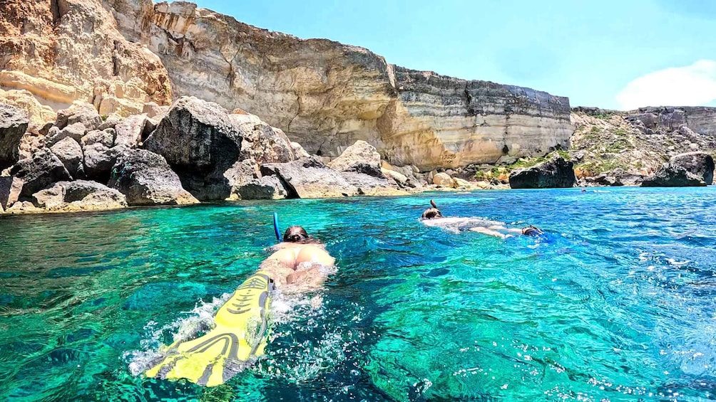 Two people snorkeling in clear blue water with rocky cliffs in the background. 4