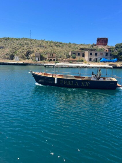 A boat named 'PERLA XX' on calm water with a hilly landscape in the background. 4