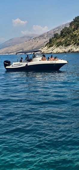 A boat named 'QUICKSILVER 500' with 'PERLA X' on its side, sailing on a calm sea with a mountainous coastline in the background. 2
