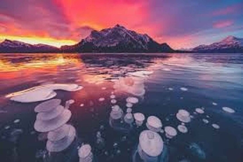 A mountain range at sunset with icebergs floating in the water. 1