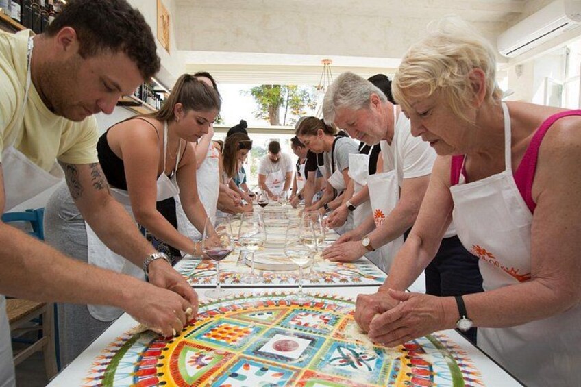 Een groep mensen doet mee aan een creatieve activiteit, mogelijk een workshop, met een kleurrijke tafelkleed en diverse knutselmaterialen. 5