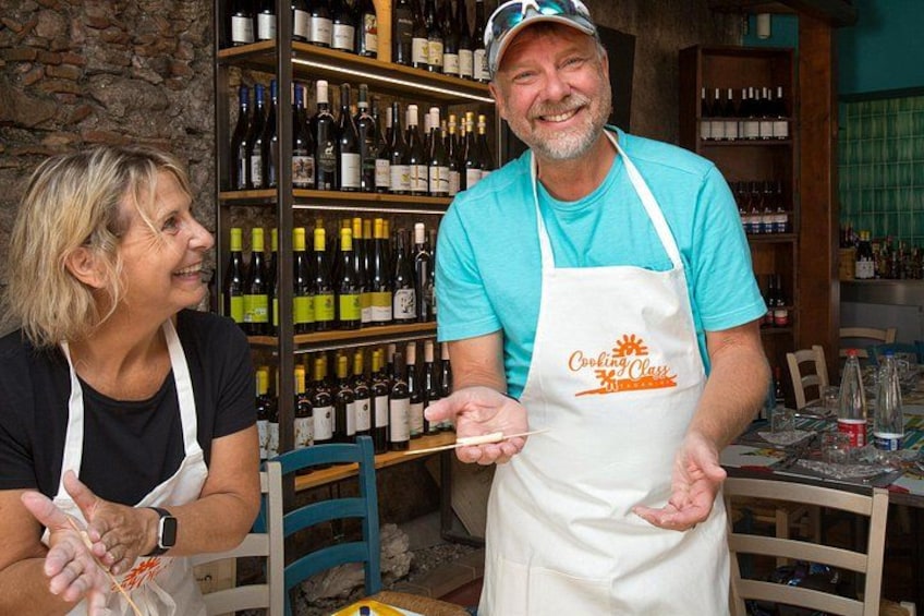 Twee personen in een keuken, met wijnflessen op de achtergrond. 2