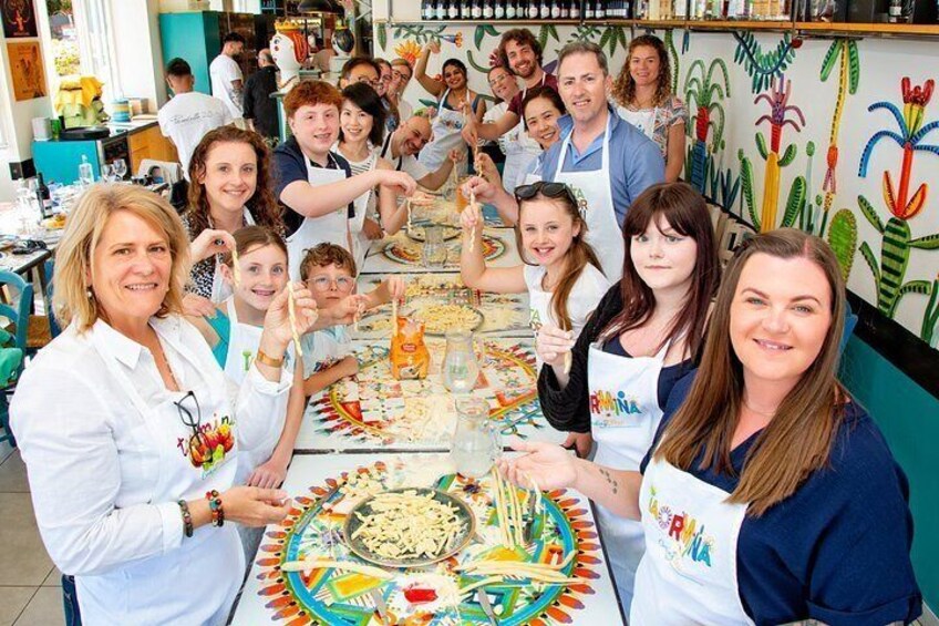 Un grupo de personas en una cocina, algunas con delantales, con una mesa llena de alimentos y un mural colorido en la pared. 2