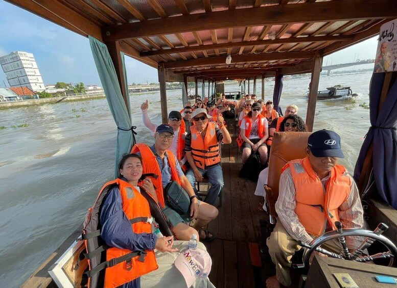 A group of people on a boat wearing life jackets, with a bridge and buildings in the background. 3