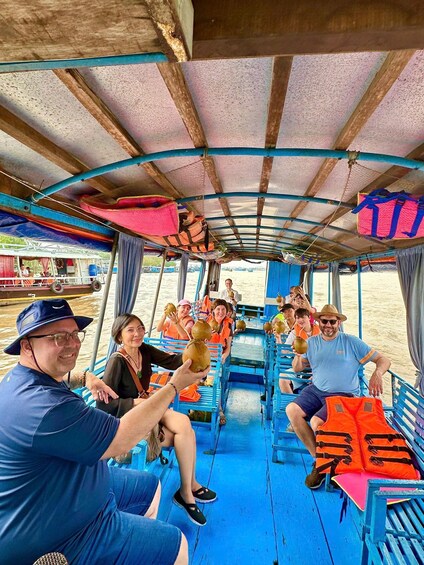 A boat with passengers holding coconuts, blue benches, and a covered deck. 1