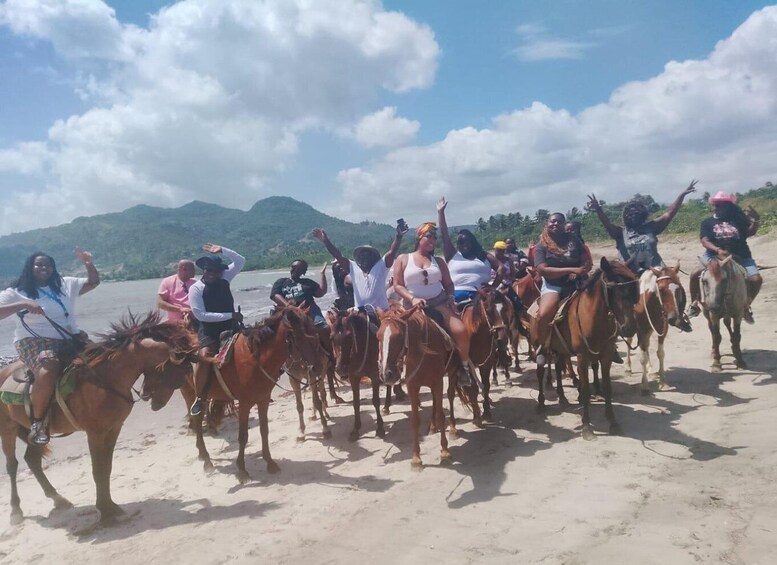 A group of people riding horses on a sandy beach with mountains in the background. 4