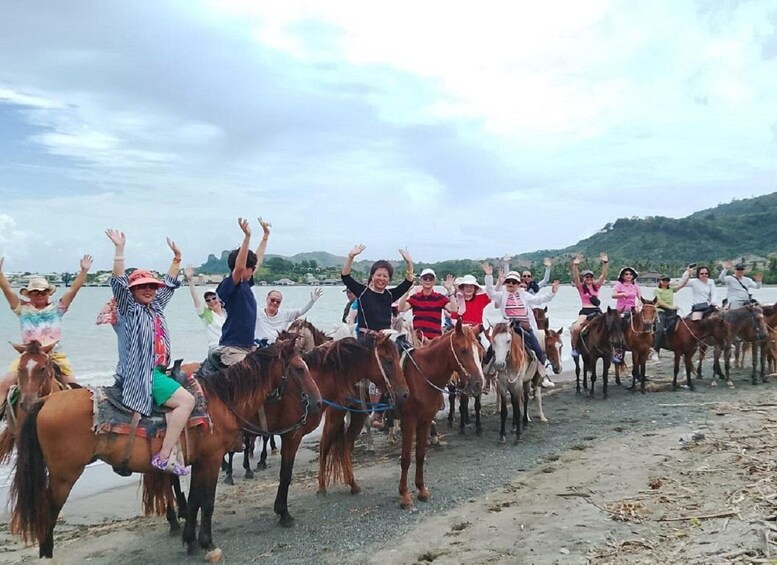 A group of people on horseback along a beach with water in the background. 2