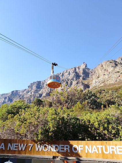 A cable car ascending a mountain with a sign reading 'A NEW 7 WONDER OF NATURE' in the foreground. 3