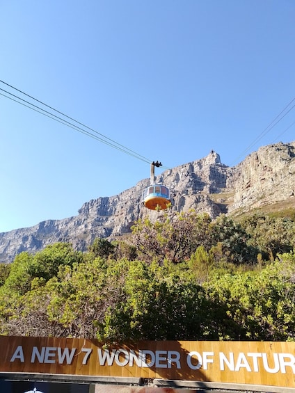 A cable car ascending a mountain with a sign reading 'A NEW 7 WONDER OF NATURE' in the foreground. 2