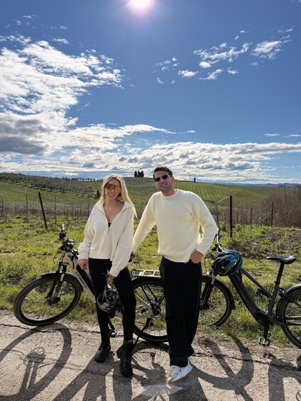 Dos personas de pie en un campo con bicicletas, cielo despejado y árboles a lo lejos. 4