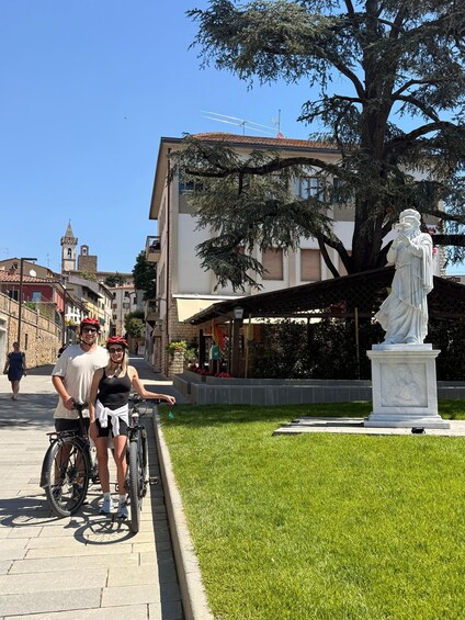 Una pareja en bicicleta, una estatua y un edificio con una torre. 3