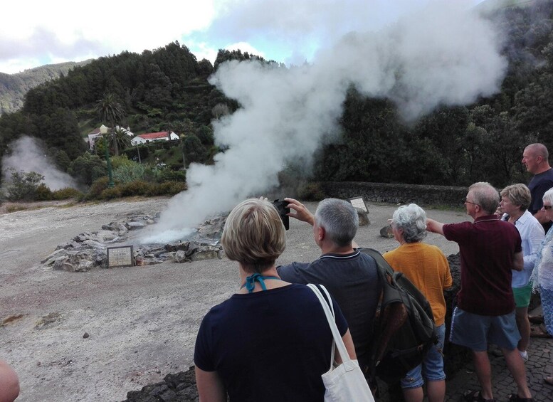 A group of people observing a steam venting from a geothermal area with a sign indicating 'Geothermal Activity'. 5