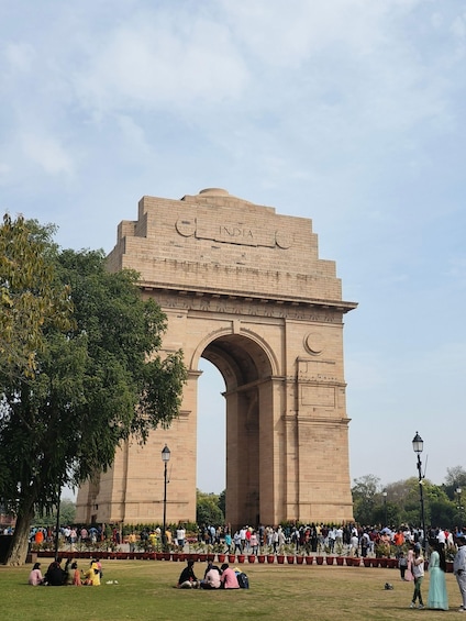 The India Gate with inscriptions and an archway, surrounded by a crowd and greenery. 5