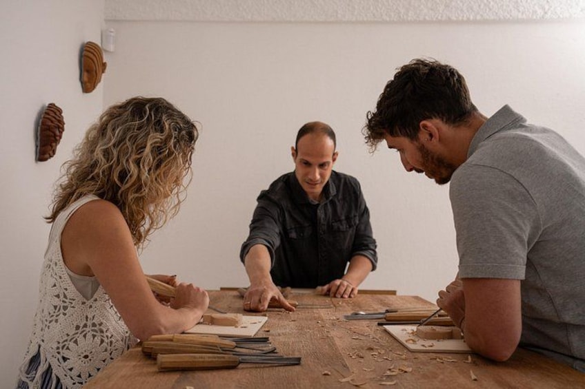Three people engaged in woodworking at a table with tools and wood shavings. 1