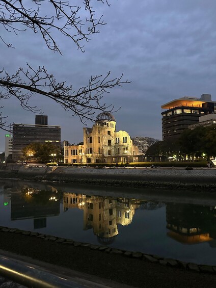 A historic building with a dome, reflected in a calm body of water, surrounded by modern buildings and a clear sky. 1