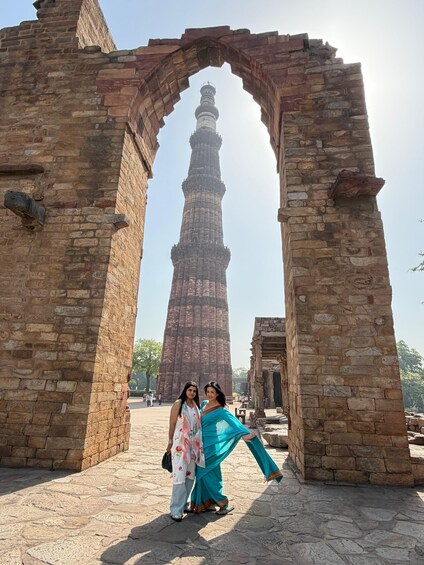An ancient tower with a spiral staircase, framed by stone arches, and two people standing in front. 3