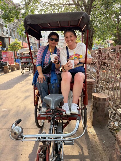 Two people sitting on a rickshaw with a street and buildings in the background. 2