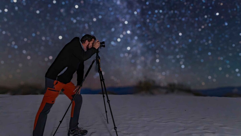 A person using a camera on a tripod in a snowy landscape with a starry night sky. 5