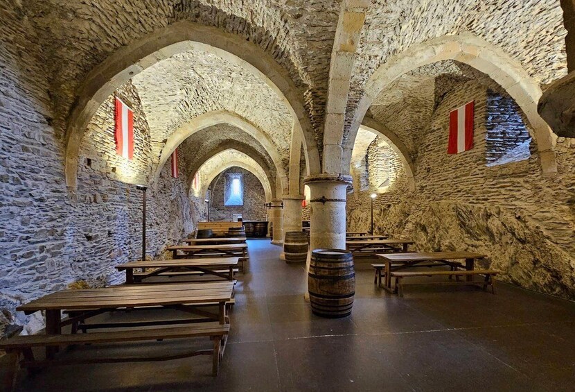 A stone-walled interior with wooden benches and barrels. 4
