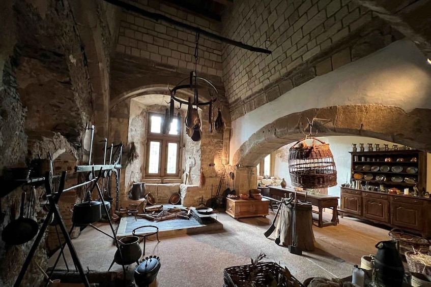 A rustic kitchen with stone walls, hanging pots, and wooden furniture. 3