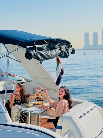 Two people on a boat with a table set for a meal, a flag, and a city skyline in the background. 1