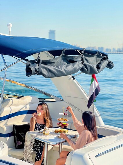 Two people on a boat with a table set for a meal, a flag, and a city skyline in the background. 5
