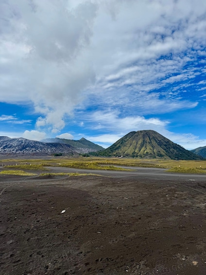 A barren landscape with a dirt road, a mountain, and a cloudy sky. 5