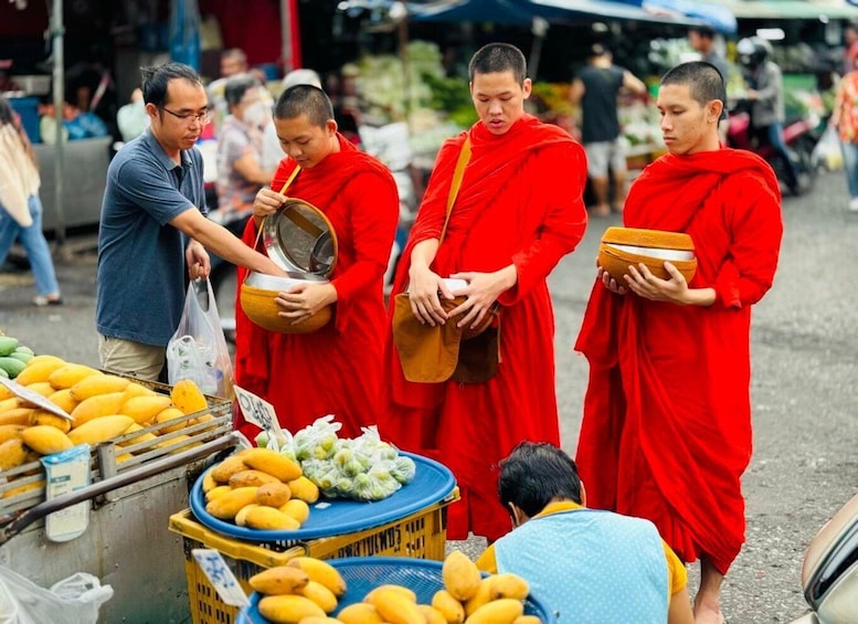 Monks in red robes at a market, holding bowls and interacting with a vendor. 1