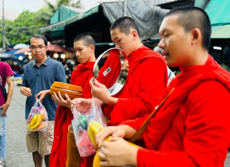Monks in red robes holding bananas and a bowl. 3