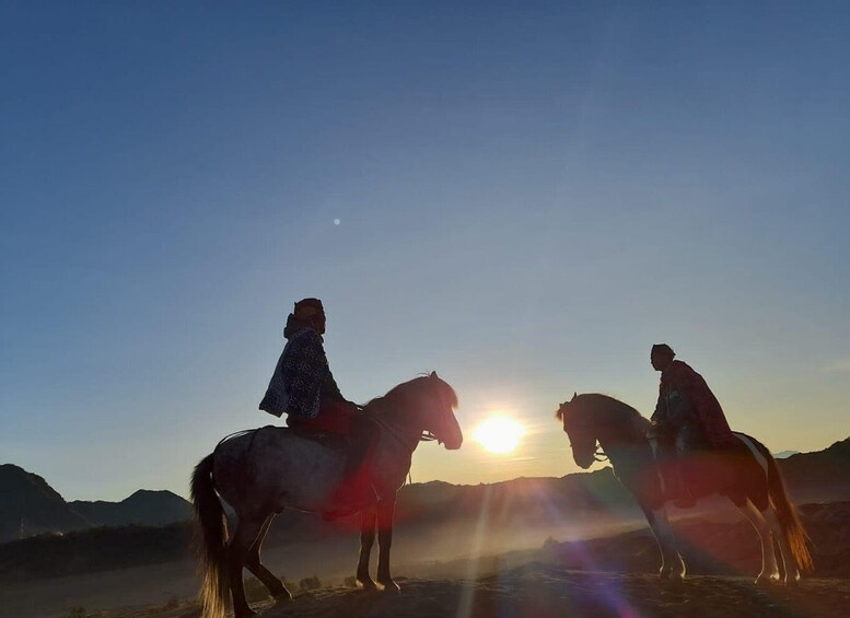 Two people riding horses in a desert landscape with the sun setting in the background. 4