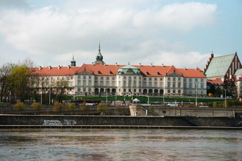 A historic building with a red roof and green spire, located beside a river. 3
