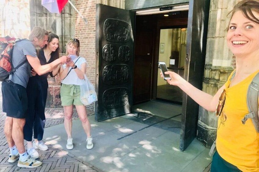A group of people standing outside a building with a large door, one person holding a smartphone. 2