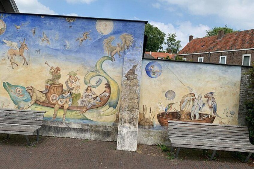 A mural with fantastical creatures and boats, benches in front, and a brick wall. 3