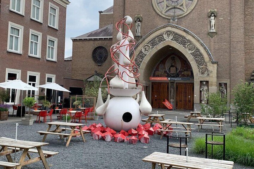 A courtyard with a large white sculpture, red chairs, and tables. 4
