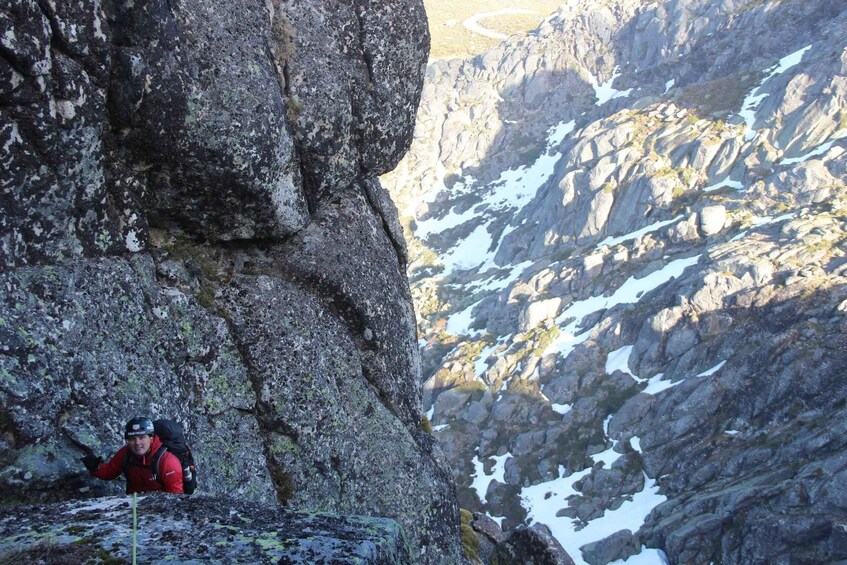 A person climbing a rocky mountain with patches of snow. 3