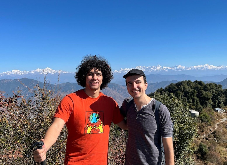 Two people standing on a hill with a mountainous landscape in the background. 1
