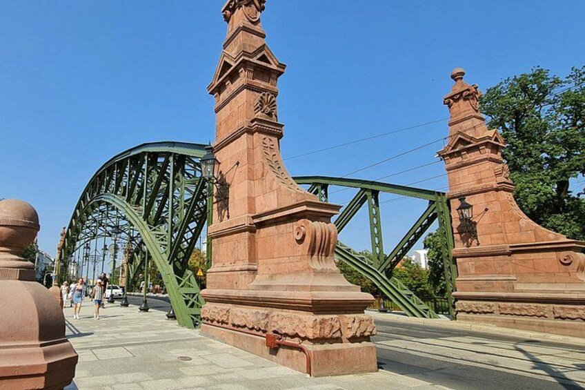 Un puente de metal verde con pilares de piedra y un cielo azul despejado. 4