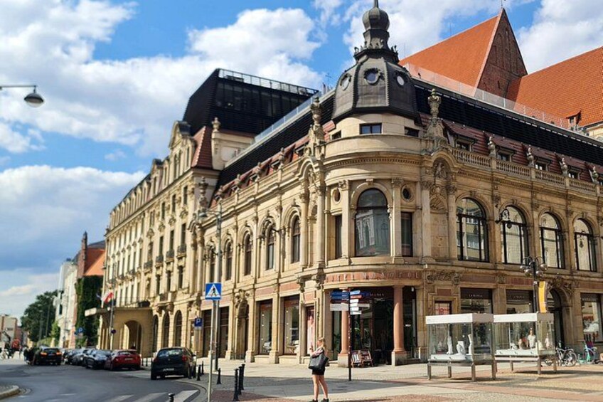 En historisk bygning med detaljeret arkitektur, et sporvognsstoppested og parkerede biler. 2