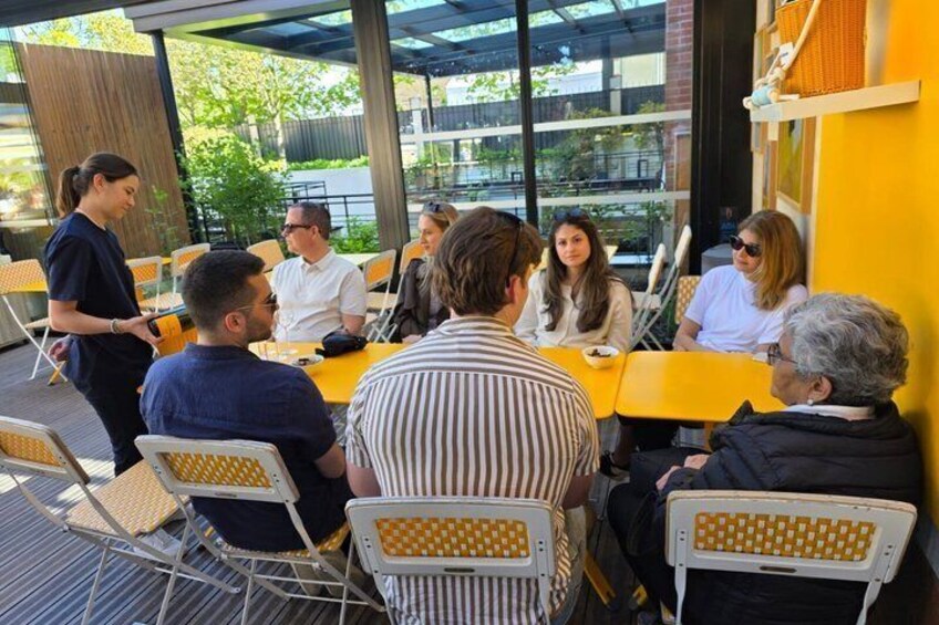 A group of people seated at yellow tables outdoors, engaged in conversation. 3