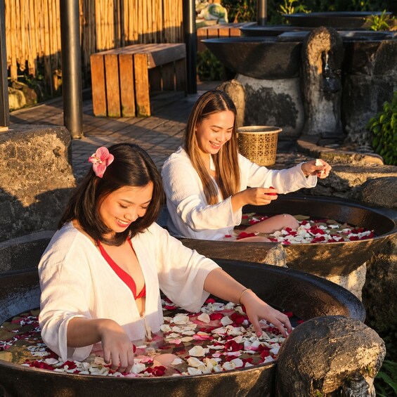 Two women performing a ritual with flower petals in large stone basins outdoors. 4
