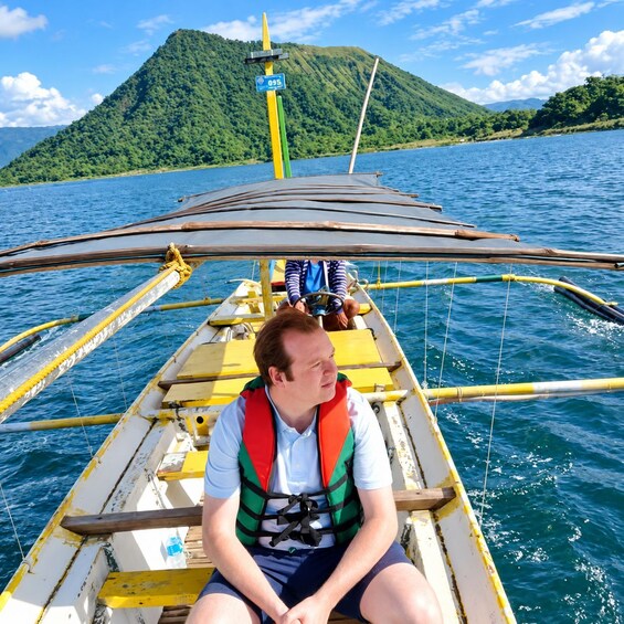 A person on a traditional boat with a mountainous landscape in the background. 2
