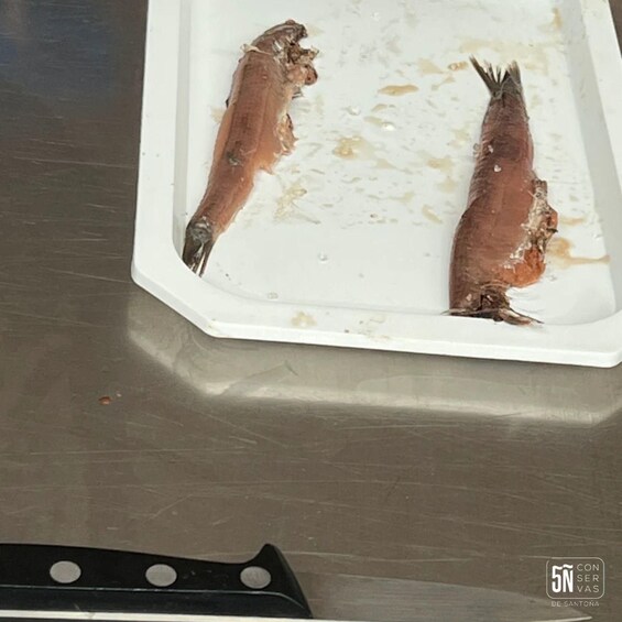 Two fish on a white tray with a knife on a metallic surface. 4