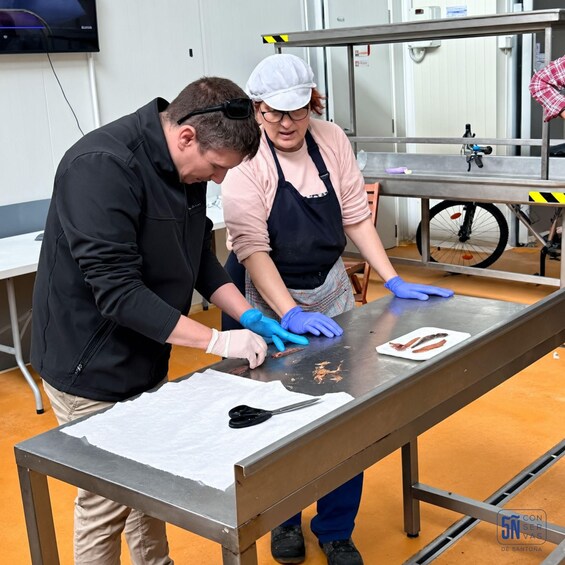 Two people working at a stainless steel table, one wearing a white cap and apron, the other in a black jacket. 5