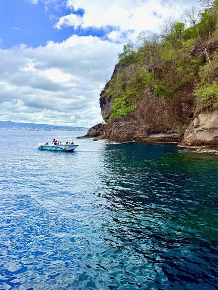 A boat on a calm sea with a rocky cliff and greenery on the shore. 3